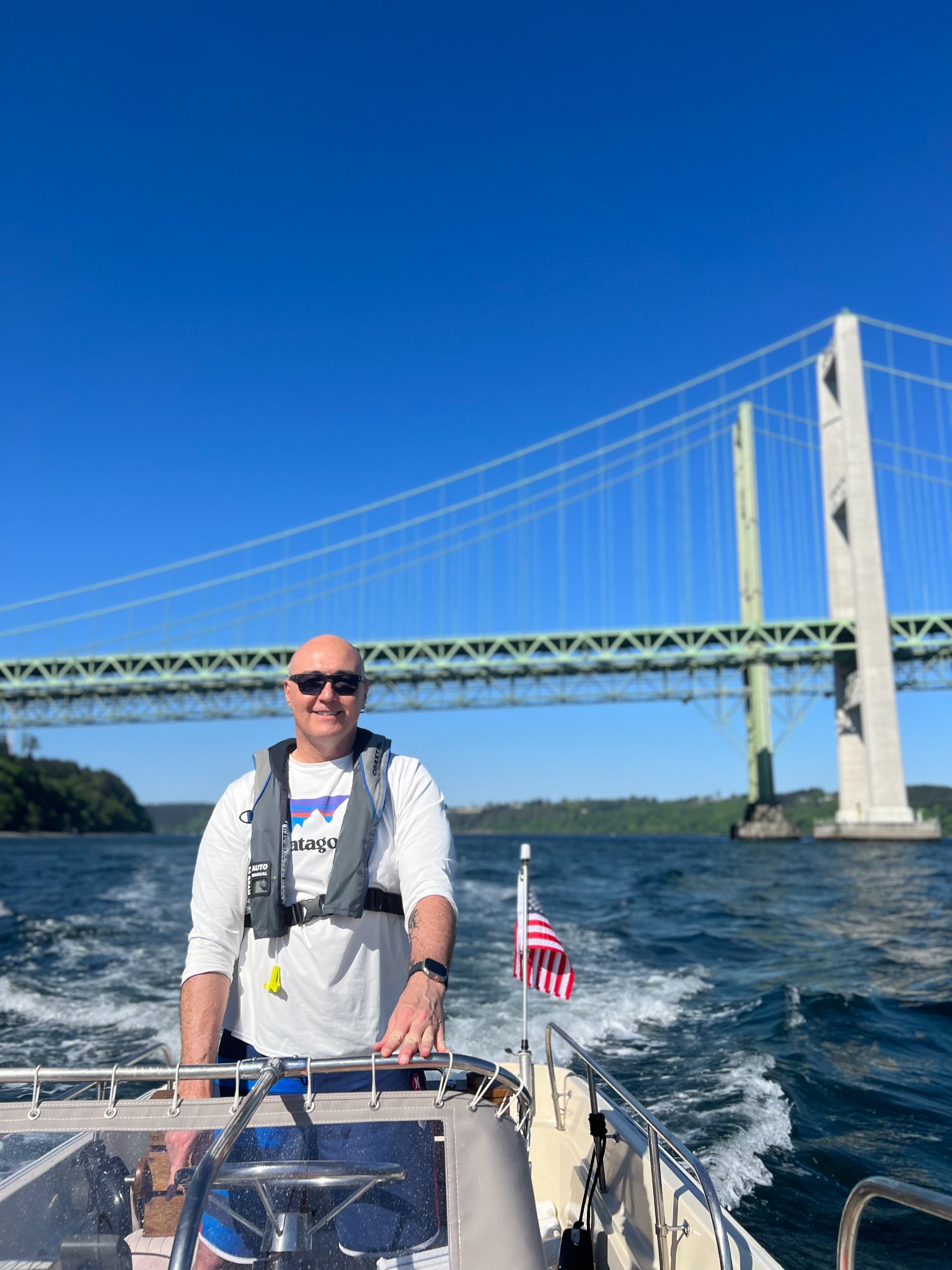Mark Dorsey at the helm of his Katama in the South Sound, with the Tacoma Narrows Bridge in the background.