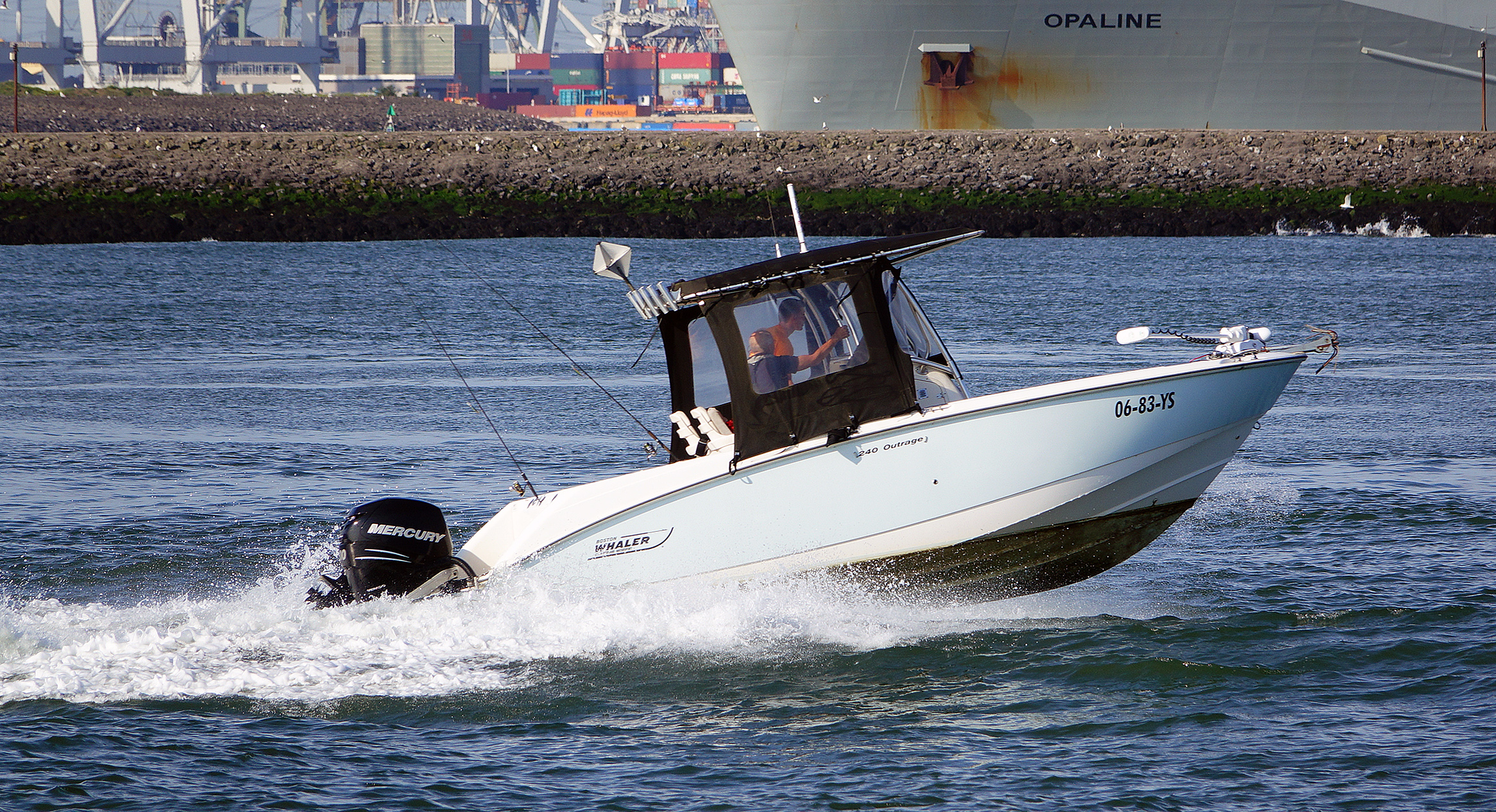A white Boston Whaler 240 Outrage underway on the Nieuwe Waterweg, with a center console, dark canopy, and a Mercury outboard.